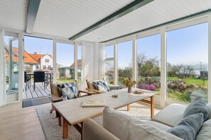 A spacious room with a large table, comfortable seating, and large windows offering a view of the outdoors.