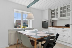 A modern kitchen with white cabinetry, a dining table with chairs, and a window with a view of buildings.