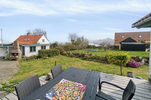 A patio with a table and chairs, a stone fireplace, and a view of a house and landscape.