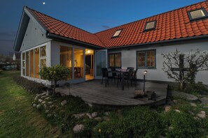 A modern house with a red-tiled roof, large windows, and a wooden deck.