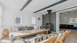 A modern living room with a fireplace, a sofa, a dining table, and a large window. - Holiday home in Årsdale with sea view (Svaneke)