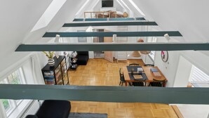 A loft-style room with a wooden floor, a dining area with a table and chairs, a TV on a shelf, and a staircase leading to an upper level. - Holiday home in Årsdale with sea view (Svaneke)