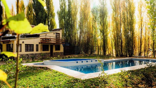 Zona de piscina amb una casa al fons, envoltada d'arbres.