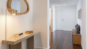 Ein moderner Flur mit einem spiegelnden Holzbettrahmen, einer Leuchte, einer kleinen Bank und einer Tür am Ende.