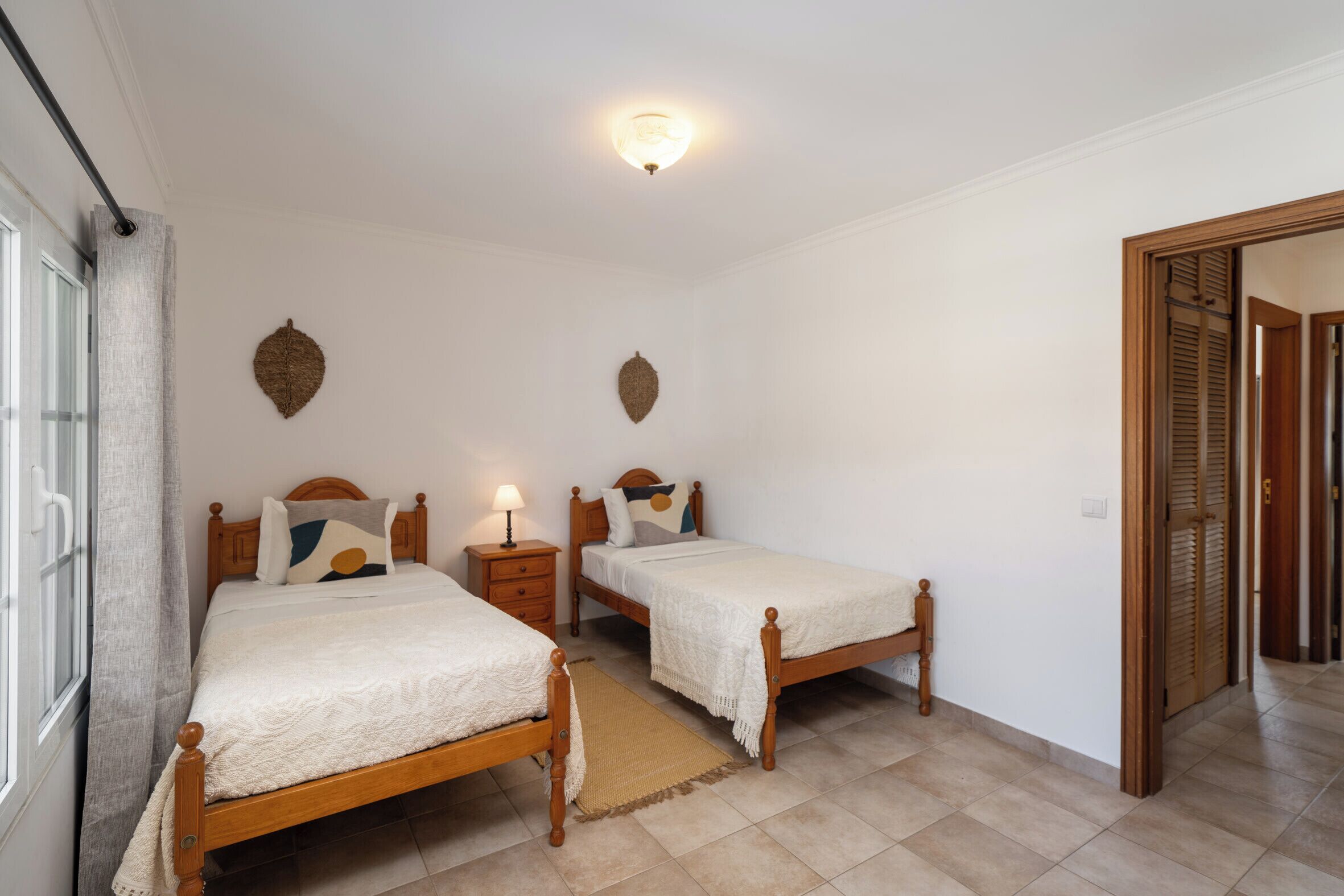 Una camera da letto con due letti in legno, un comodino con una lampada, un tappeto tessuto e una lampada a sospensione al soffitto.