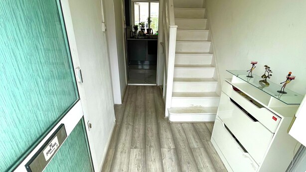 Un corridoio stretto con pavimento in legno, una porta in vetro, una scala e una piccola mensola con oggetti decorativi.