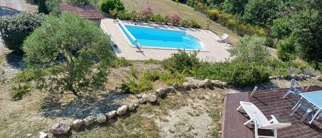 An aerial view of a swimming pool surrounded by a wooden deck with lounge chairs.