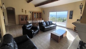 Amplia sala de estar con sofás de cuero, una mesa de centro de madera y un comedor con mesa y sillas. Se ve una escalera al fondo, que conduce a un piso superior.