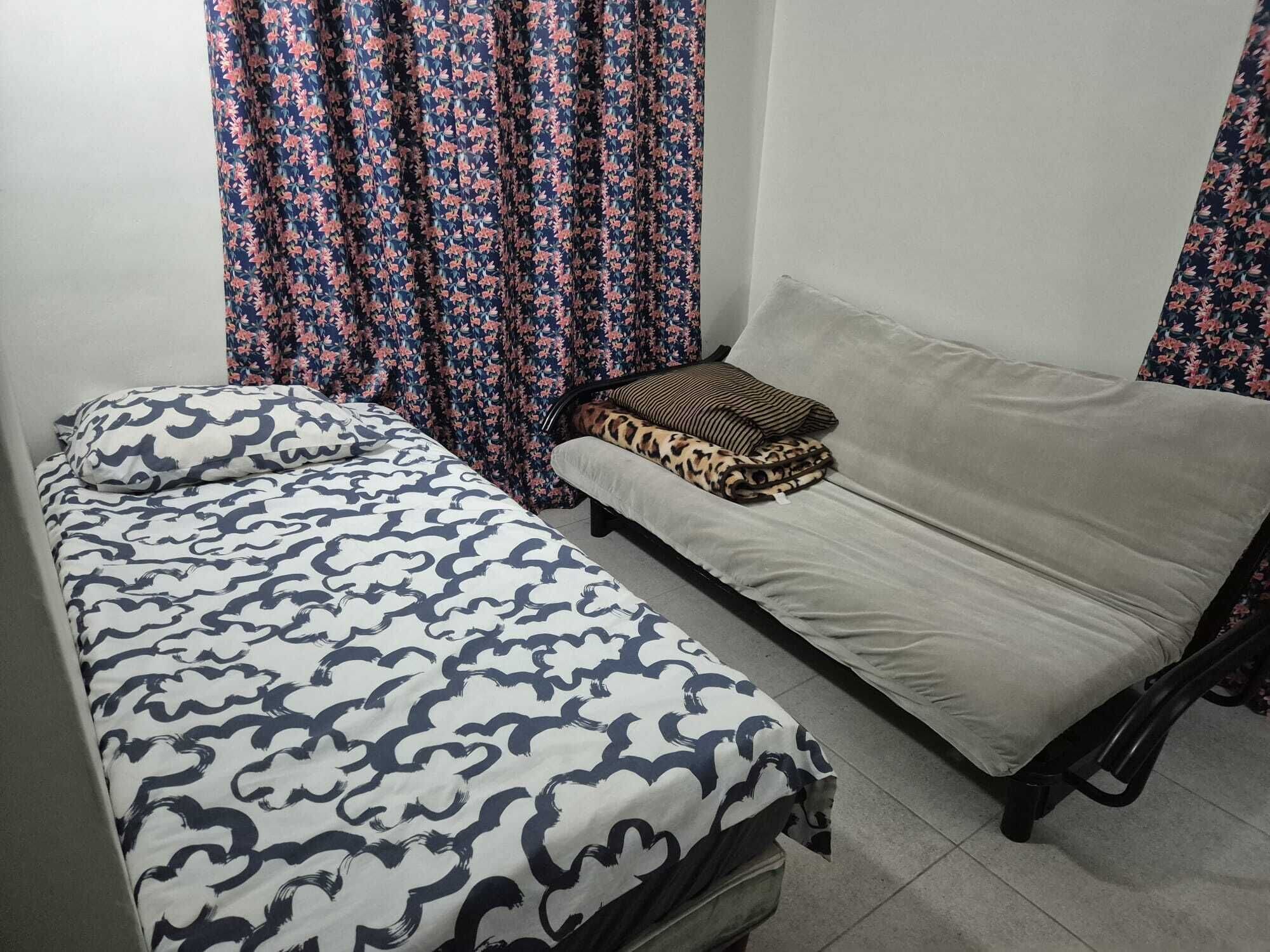 A single bed with a patterned bedspread, a sofa with a leopard print cushion, and floral curtains.