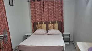 A bedroom with a bed, curtains, a bedside table, a lamp, and a dresser.