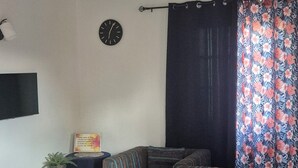 A living room with a sectional sofa, a small table, a clock, and a curtain with a floral pattern.