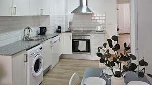 A modern kitchen with white cabinets, a built-in oven, a washing machine, and a dining area with a table set for two. - Chic Escape Apartment (Godella)