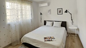 A bedroom with a bed, a small table, a lamp, and an air conditioning unit. - Chic Escape Apartment (Godella)