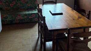 A dining area with a wooden table and chairs, a floral sofa, and a window with a view of greenery. - House in a quiet mountain village (Lus La Croix haute)