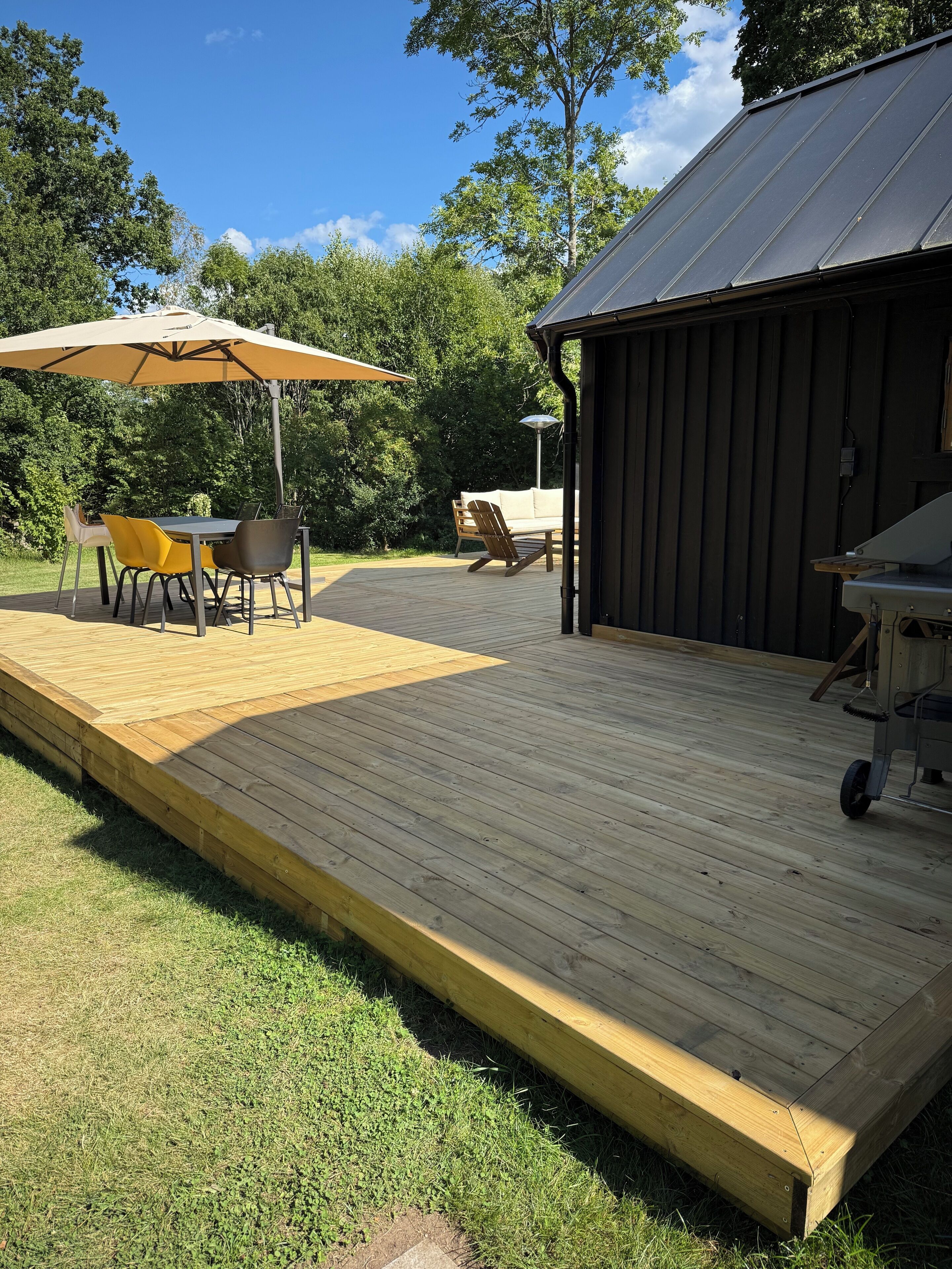 A wooden deck with a table and chairs, a covered patio area, and a building with a metal roof.