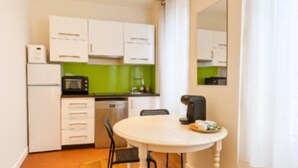 A compact kitchen with white cabinets, a microwave, a coffee maker, and a dining table with chairs.