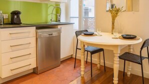 A compact kitchen with white cabinets, a dishwasher, and a dining table with chairs.
