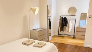 A bedroom with a bed, a bedside table with a vase, a mirror, a clothing rack, and a dresser.