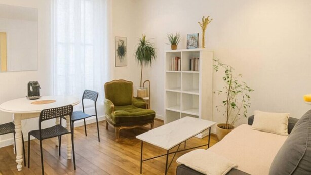 A modern living room with a wooden floor, a grey sofa, a green armchair, a white coffee table, and a bookshelf.