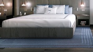 Ein modernes Schlafzimmer mit einem großen Bett, einem Holzkopfende, Nachttischlampen und einem blauen Teppich.