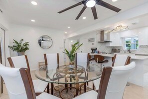 Una cocina moderna con armarios blancos, una mesa de comedor de vidrio y un ventilador de techo.