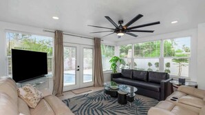 A living room with a sofa, a coffee table, a TV, and a ceiling fan. - NEW! Tropical Paradise with Pool! 5 mins to beach! (St. Petersburg)