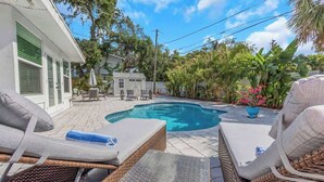A swimming pool with lounge chairs, a covered outdoor kitchen, and lush greenery. - NEW! Tropical Paradise with Pool! 5 mins to beach! (St. Petersburg)
