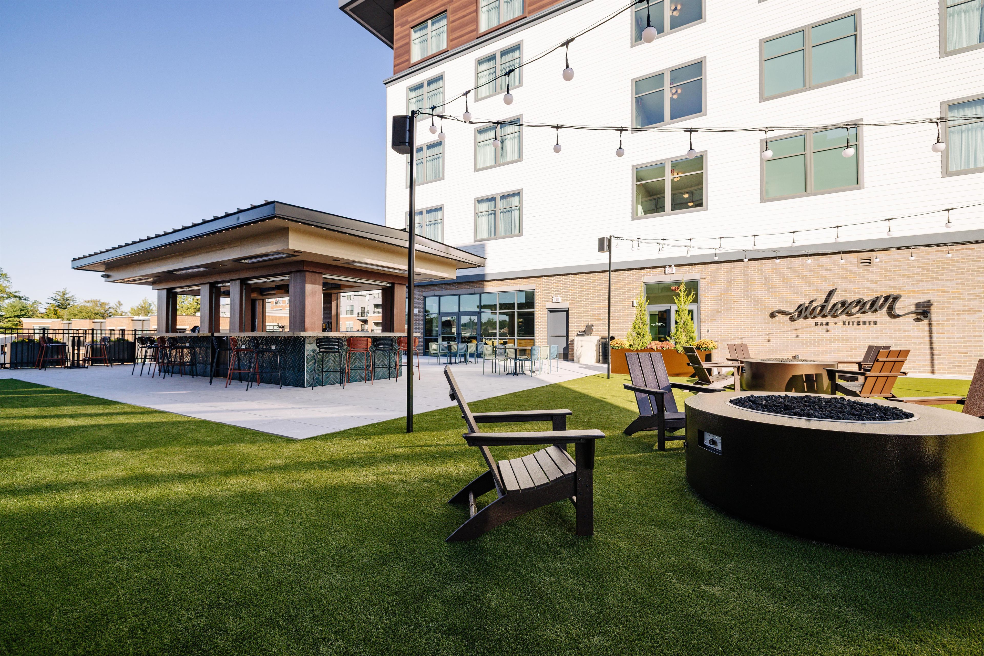 An outdoor seating area with a fire pit, chairs, and a bar area with a sign reading 'Saloan Bar + Kitchen'.