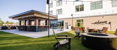 An outdoor seating area with a fire pit, chairs, and a bar area with a sign reading 'Saloan Bar + Kitchen'.
