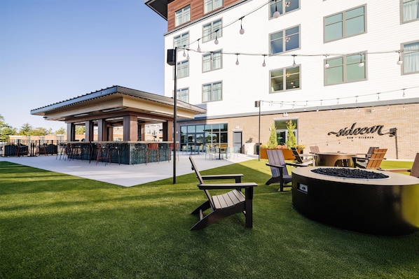 An outdoor seating area with a fire pit, chairs, and a bar area with a sign reading 'Saloan Bar + Kitchen'. - The Hotel Rambler Montgomery, Tapestry Collection By Hilton (Montgomery)