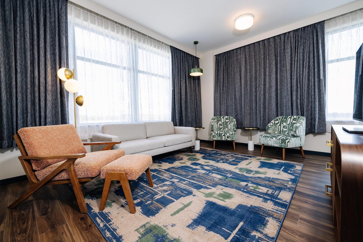 A modern living room with a sofa, two armchairs, a patterned rug, and a wooden floor.