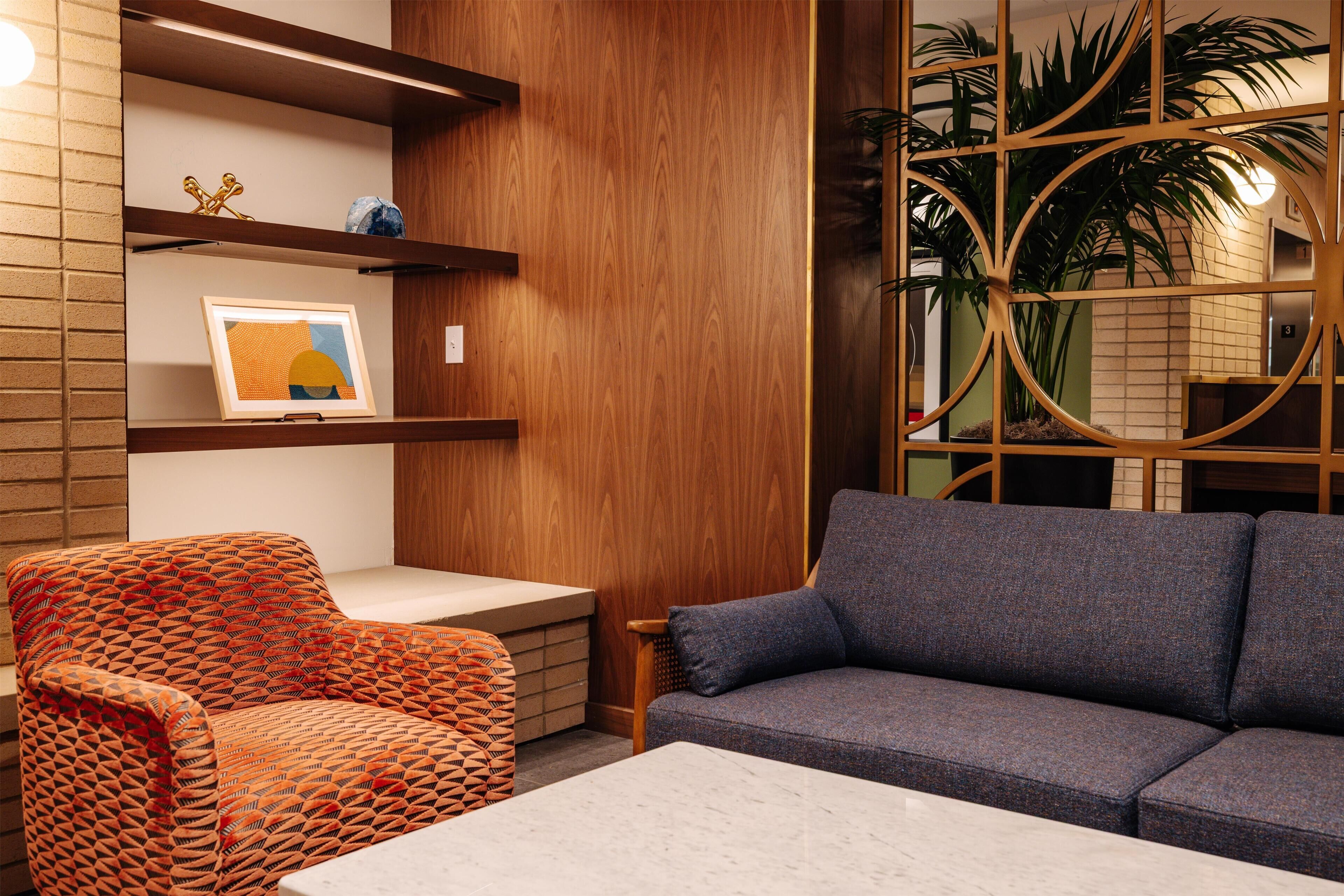 A modern interior with a wooden panel wall, a grey sofa, an orange patterned chair, and a small table.