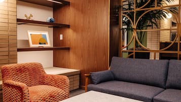A modern interior with a wooden panel wall, a grey sofa, an orange patterned chair, and a small table.