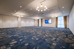 A large conference room with a patterned carpet, recessed ceiling lights, and a flat-screen TV mounted on the wall.