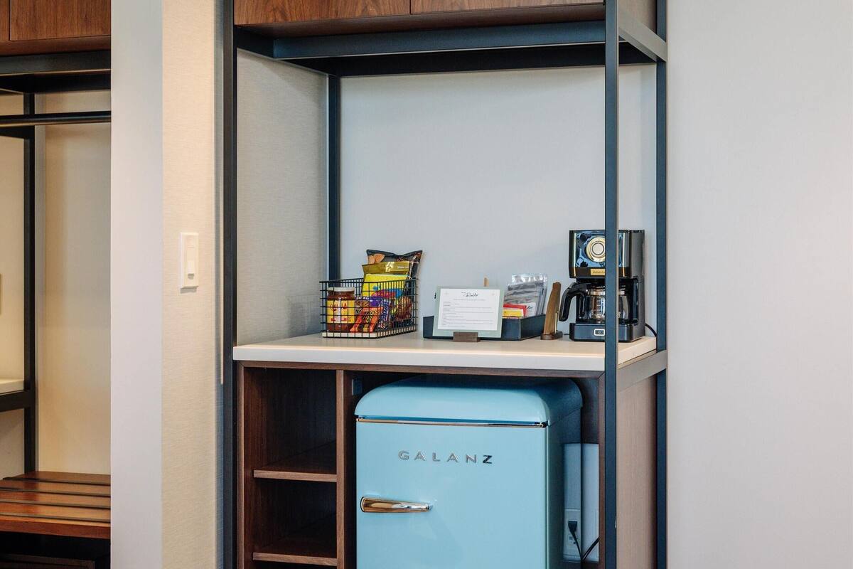 A compact kitchenette with a blue refrigerator, wooden cabinets, and a coffee maker.
