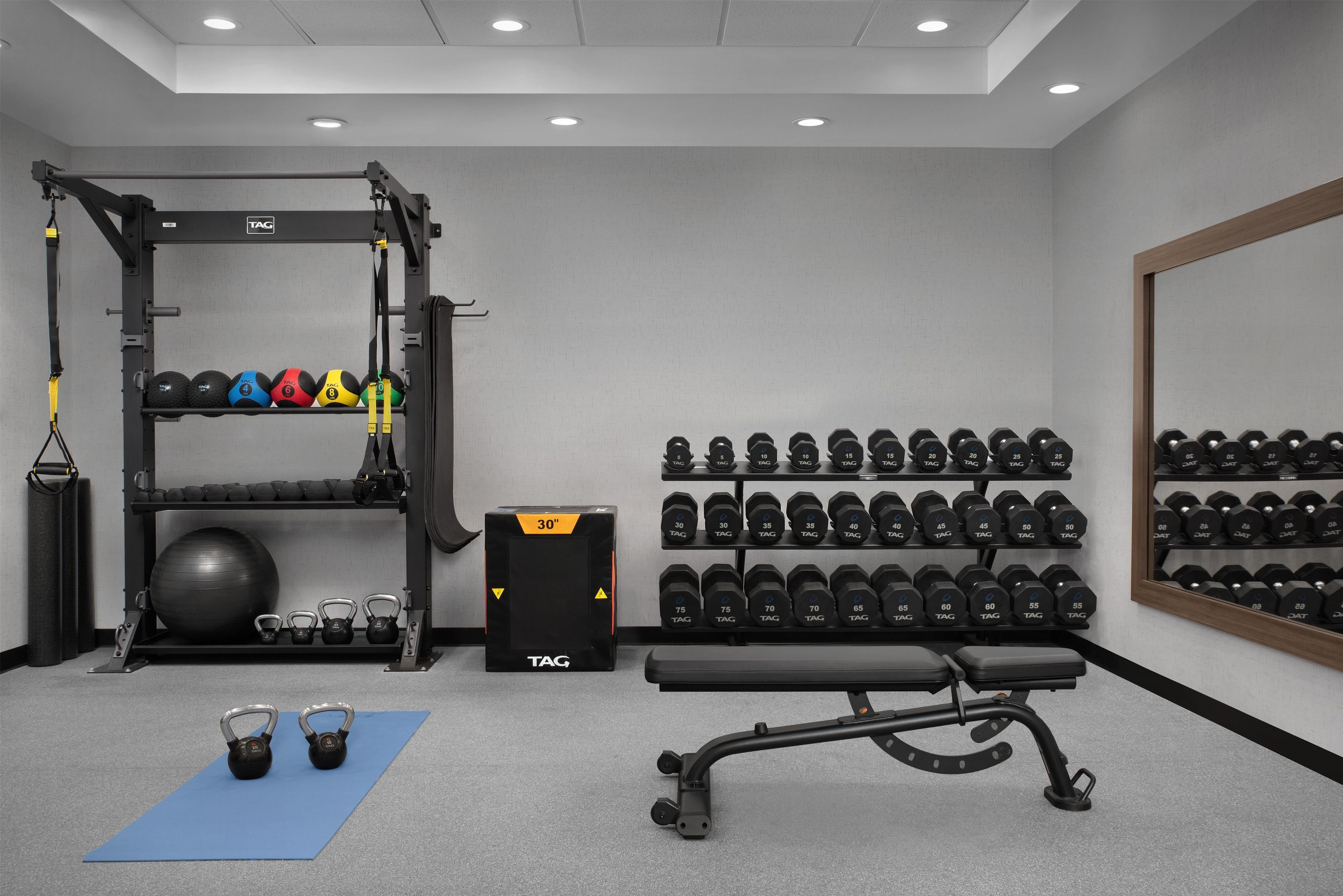 A gym with a squat rack, kettlebells, a bench, and a wall of dumbbells.