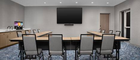 Un salón de conferencias con una mesa larga, sillas, un televisor de pantalla plana y una puerta.