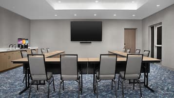 Un salón de conferencias con una larga mesa, seis sillas, un televisor de pantalla plana y una estación de café.