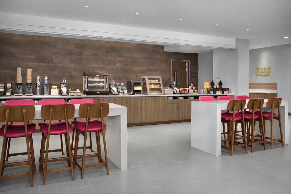 A modern cafe with a wooden counter, espresso machines, and pink chairs.