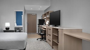 Una habitación de hotel moderna con cama, escritorio, silla, televisión y puerta que da a un baño.