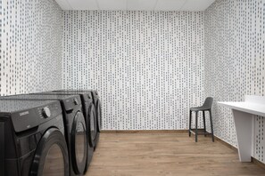 Une buanderie équipée d’un lave-linge et d’un sèche-linge, avec un plancher en bois et un mur blanc orné d’un motif.