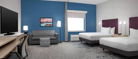 Una habitación de hotel con escritorio, dos camas, televisor, sofá y ventana con cortinas.