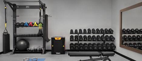 Un gimnasio con una estructura para sentadillas, picos de mancuerna, un banco y una pared llena de mancuernas.