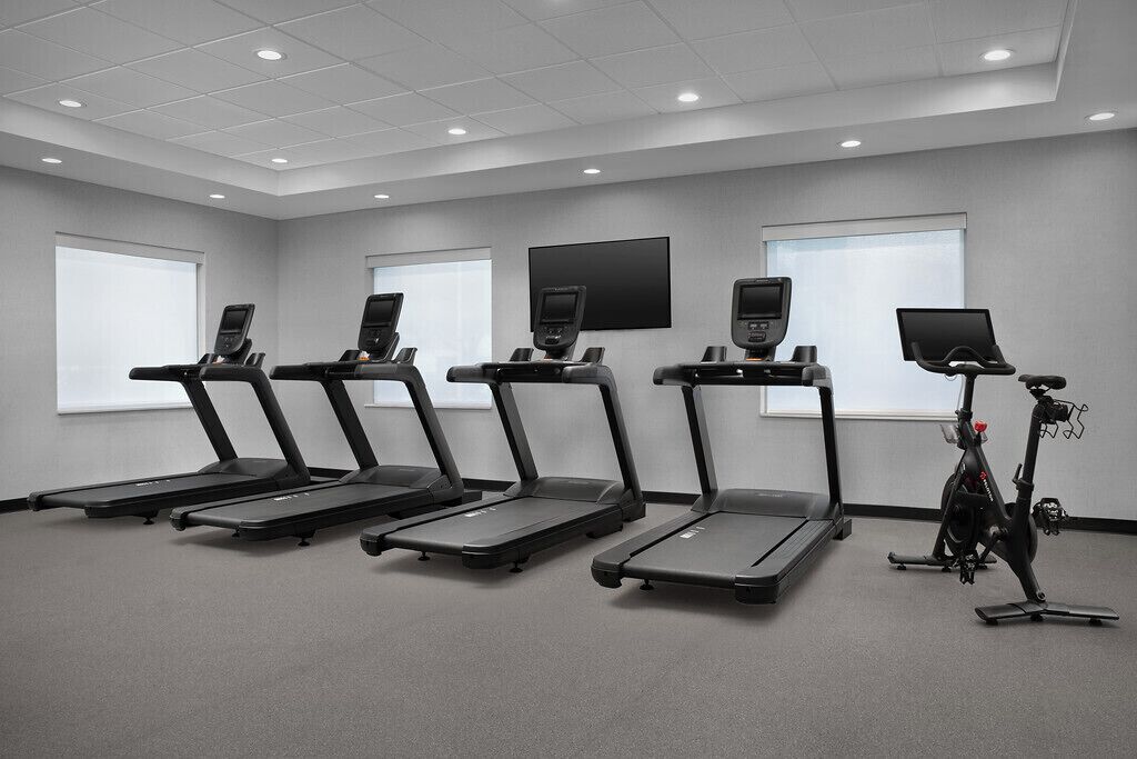 A fitness room with treadmills, a stationary bike, and a wall-mounted screen.