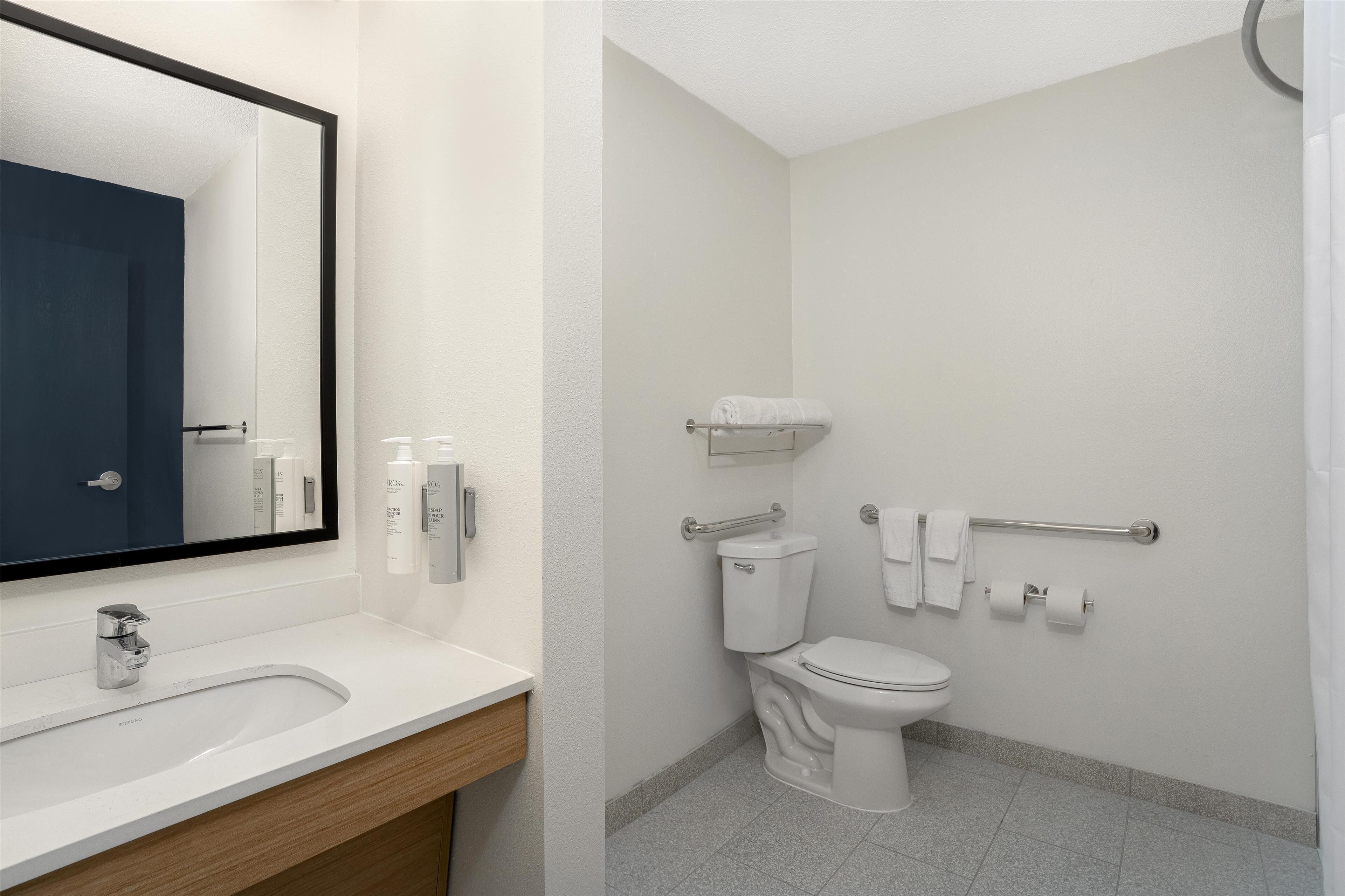 Un baño moderno con un lavamanos blanco, un espejo, un inodoro y un perchero para toallas.