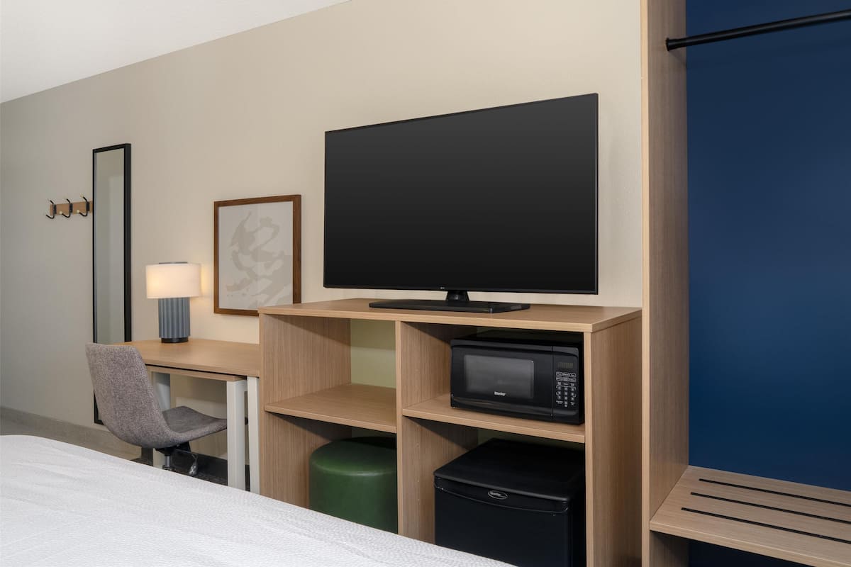 Une chambre d’hôtel équipée d’un lit, d’un bureau avec un ordinateur, d’une télévision à écran plat, d’un four à micro-ondes et d’une poubelle.