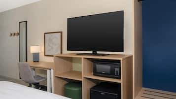 Ett hotellrum med en säng, ett skrivbord med en dator, en platt-TV, en mikrovågsugn och en papperskorg.