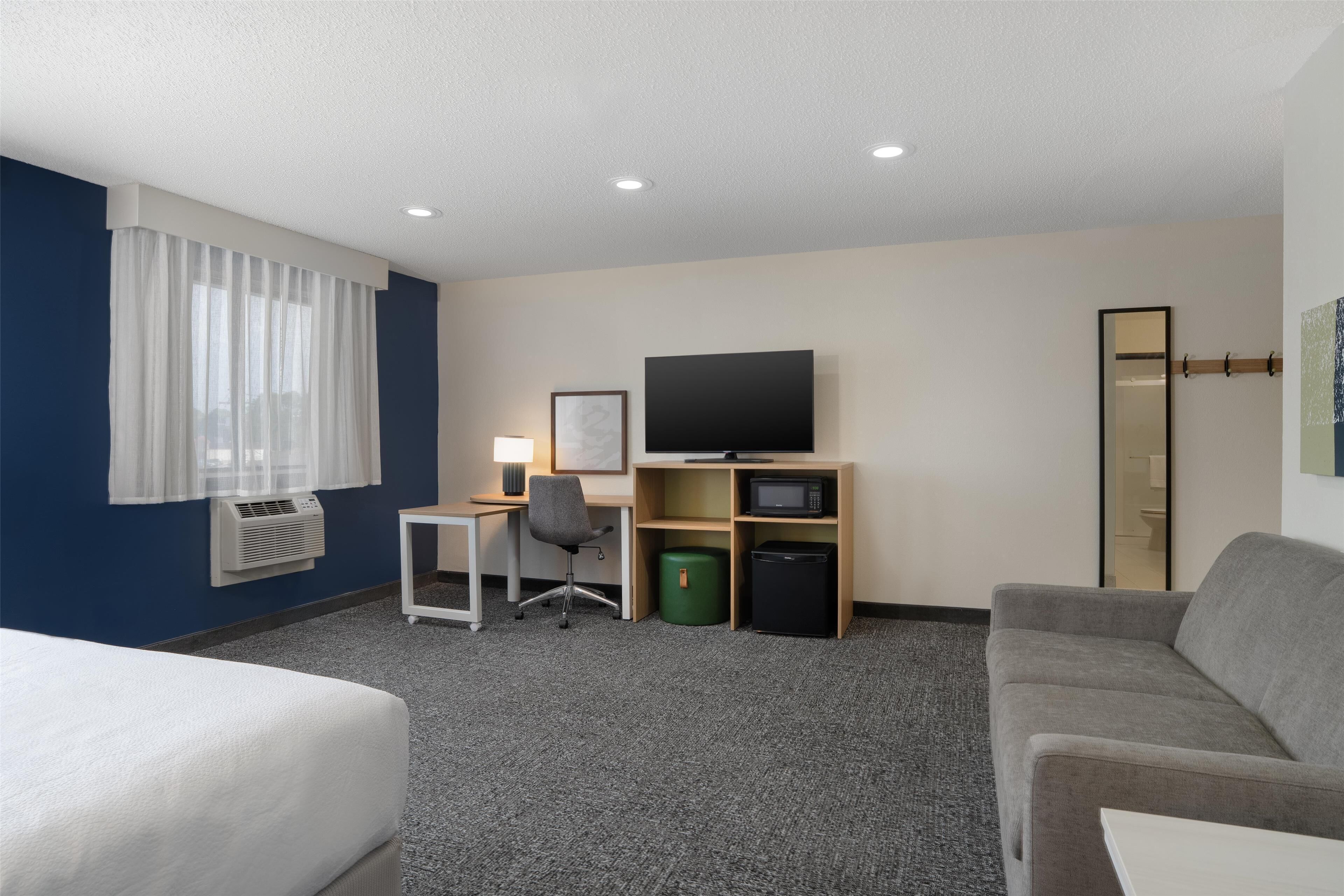 A hotel room with a bed, a desk with a computer, a television, a mirror, and a couch.