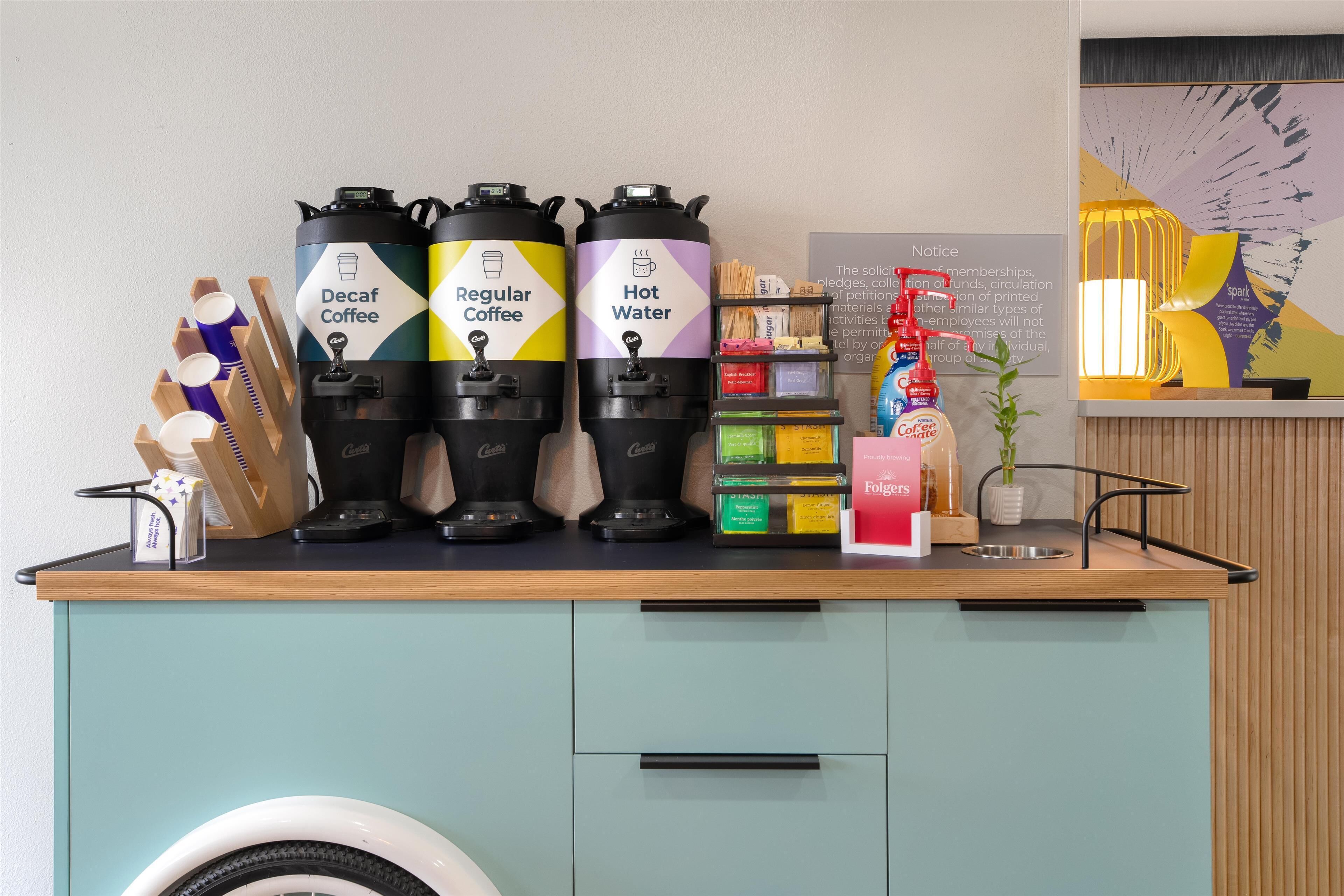 A coffee station with Decaf Coffee, Regular Coffee, and Hot Water dispensers, a coffee machine, and a variety of coffee pods.