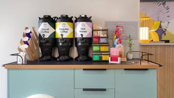 A coffee station with Decaf Coffee, Regular Coffee, and Hot Water dispensers, a coffee machine, and a variety of coffee pods.